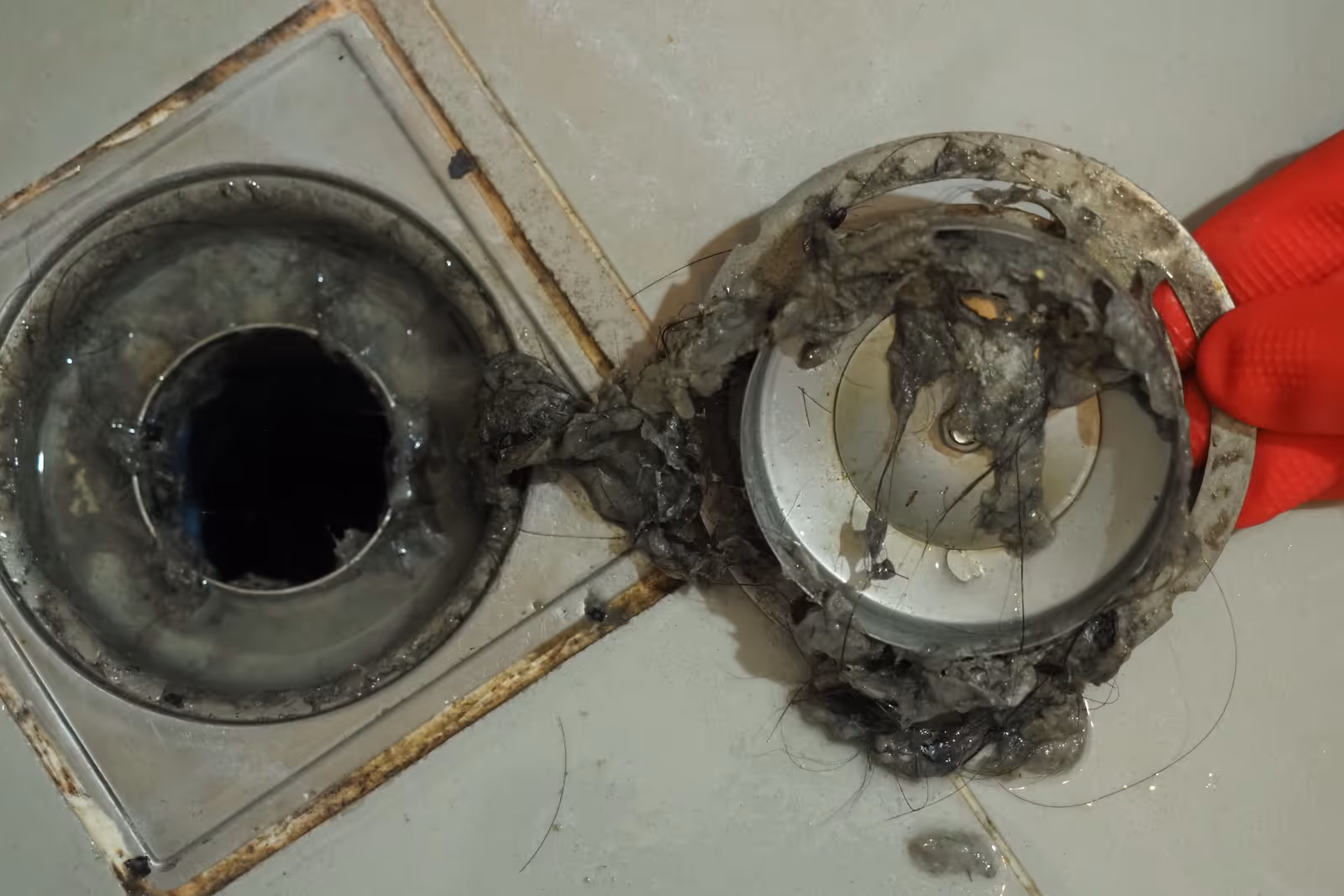 Close-up of a clogged drain with water pooling and visible hair tangled in the blockage.