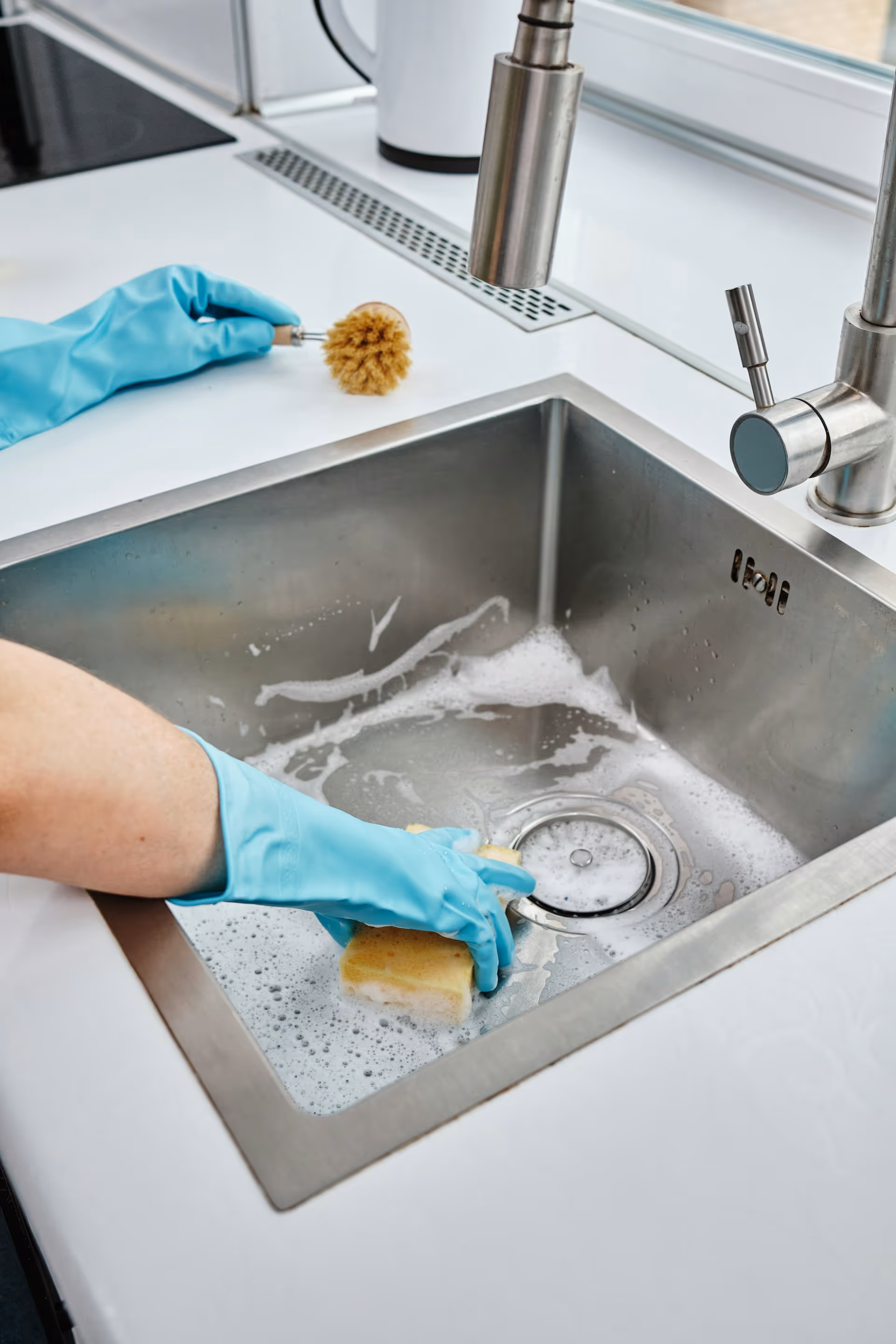 Person cleaning a sink around the drain area with a cloth and blue gloves.